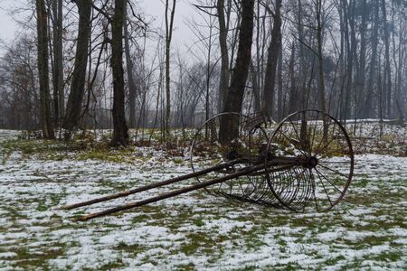 Horse rake lies on the ground, covered with snow, against the background of trees in the fogの写真素材
