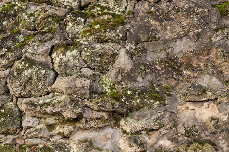Stone texture at the foot of a mountain or cliff or cave wall, dotted with grooves and covered with mossの写真素材