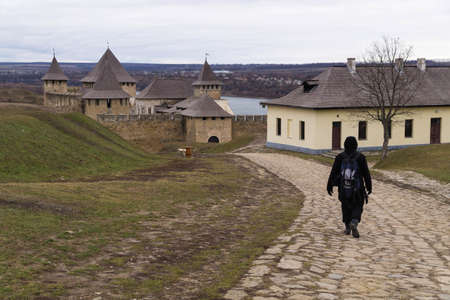 Male tourist with a backpack goes along a cobblestone road towards Khotyn fortress