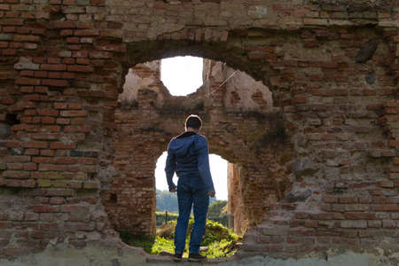 A young man in blue clothes stands on the ruins of an old Golshany castle, turning his back, framed by a round hole in the castle wallのeditorial素材