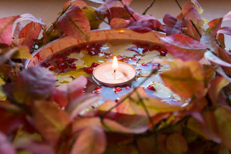 Autumn candlestick: a lit candle in a bowl of water, rowan berries and yellow maple leaves surrounded by branches with red foliageの写真素材