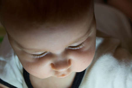 A half-year-old child in a white bodysuit with downcast eyes, with a face illuminated from below, close-upの写真素材
