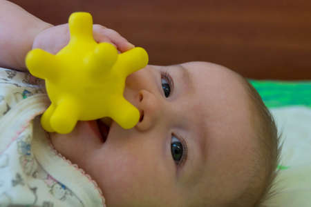 A half-year-old child smiles and holds in his mouth a yellow tactile ball with horns, similar to the coronavirusの写真素材