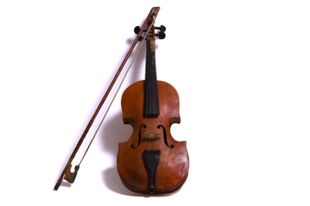 An unusual antique brown violin, roughly handmade, with peeling paint and dents, with a bow leaning against the fingerboard, photographed against a white backgroundの写真素材