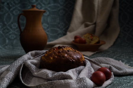In a cozy, rustic setting, a loaf of traditional easter cake is surrounded by red eggs and a clay...
