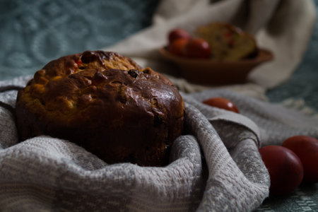 Warm easter cake sits atop a patterned cloth, surrounded by decorative items and painted red eggs in...