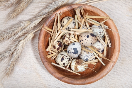 quail eggs in a wooden bowl and wheat ears on linen clothの写真素材
