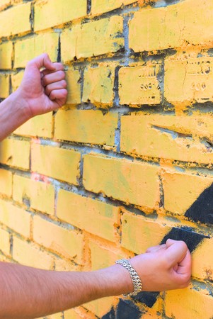 Fists of the young man are touching the wall. There is a silver bracelet on right arm.の写真素材