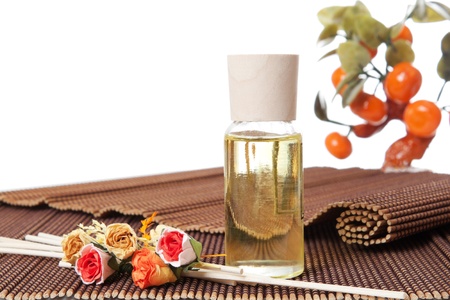 Glass bottle with yellow oil and small flowers lay on brown mat. Stone trees at the backgroundの写真素材