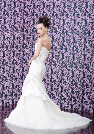 Young adult bride in white wedding dress posing over magenta wall の写真素材