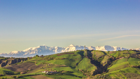 white snowy mountains behind the green hills in the countryside of Italy