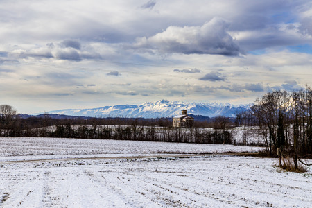 snow on the fields next to a medieval church in the italian countrysideの写真素材