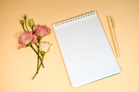 A notebook in a cage with a pen and eustoma flowers lying next to it on a beige backgroundの写真素材