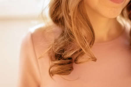 Curly blonde hair of a girl lying on her shoulder against the background of a blurry pink dressの写真素材