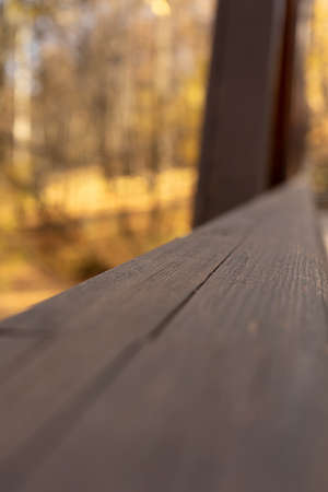 Brown wooden railing stretching into the distance against the background of a sunny autumn forest with a narrow focusの写真素材