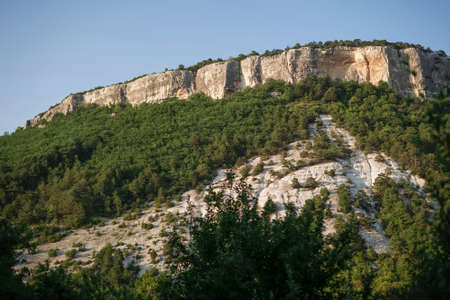 View of the cliffs of the mountain with trees growing on the slopes in the sunset lightの写真素材