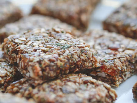 Baked grain muesli with dried fruits, nuts, honey, herbs, cut into square pieces on a white plateの写真素材
