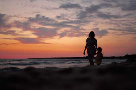 Silhouettes of a woman with a child walking along the seashore at sunsetの写真素材