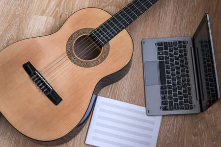 Brown guitar size, gray laptop, music notebook on a light brown wooden board backgroundの写真素材