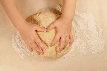 Childrens hands lie in the shape of a heart on a curd dough on a background of baking paper sprinkled with white flourの写真素材