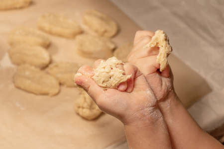 Childrens hands hold a piece of cottage cheese dough against the background of a table covered with baking paper sprinkled with white flourの写真素材