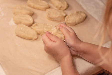 Childrens hands hold a piece of dough against the background of a table covered with baking paper sprinkled with white flour with pieces of doughの写真素材