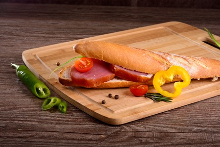 big sandwich with smoked tenderloin,lies on a wooden Board,lay next to fresh vegetablesの写真素材