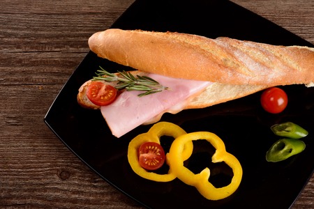 big sandwich with smoked tenderloin,lies on the black plate next to fresh vegetablesの写真素材