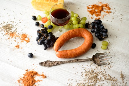 a glass of wine and grapes next to cheese and sausagesの写真素材