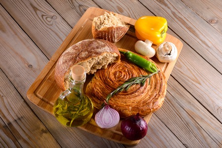 the broken bread on the Board next to olive oil and vegetables on wooden table
