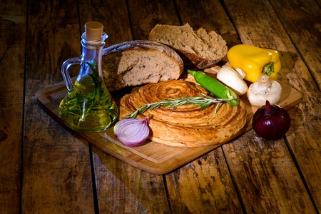the broken bread on the Board next to olive oil and vegetables on wooden tableの写真素材