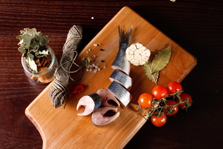 pieces of herring on a cutting Board, next to pepper and garlic and tomatoes on a branch. the view from the topの写真素材