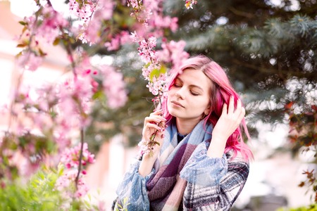young beautiful girl with pink hair standing near a tree with flowers, pink flowers, spring, sun, happiness, tendernessの写真素材