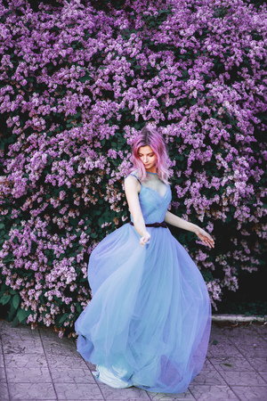 The red-haired girl dances and is spinning in a luxurious, dignified, lilac, purple dress. Fabric beautifully flies in motion. The background is a fantastic garden. Art photoの写真素材