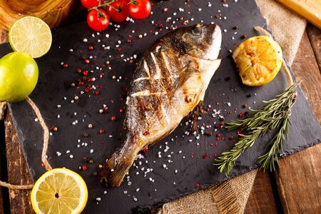 delicious roasted dorado or Gilt-head bream fish with lemon and orange slices, spices, and fresh...
