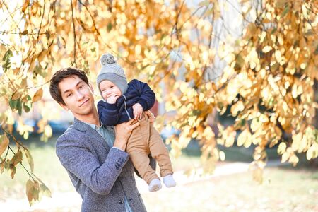 A laughing father holds a beautiful child in his arms against the background of an autumn landscapeの写真素材