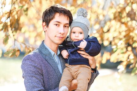 A laughing father holds a beautiful child in his arms against the background of an autumn landscape