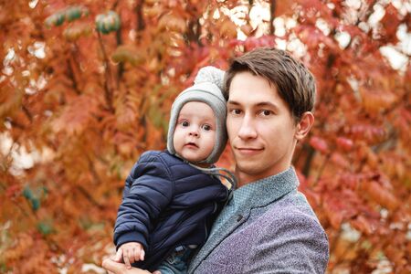 a young son is sitting in the arms of a young father on an autumn backgroundの写真素材