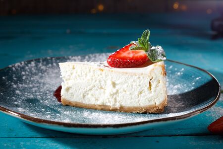 Cheesecake with strawberries on a blue plate on the background of the table