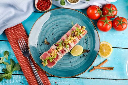 Sliced tuna steak with sesame seeds on a blue plate against a wooden tableの写真素材