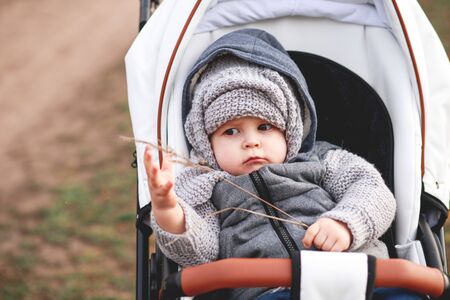 A cute little beautiful one year old boy is sitting and smiling in a stroller and waiting for his motherの写真素材