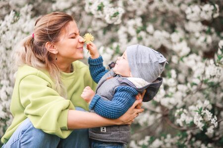 A mother plays and talks with a child against the background of a flowering tree, happy smiling...