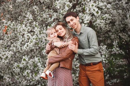 Beautiful young parents and their cute little son have fun near flowering trees, happy familyの写真素材