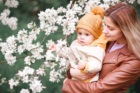 a girl with her son in her arms near a flowering Apple tree in springの写真素材
