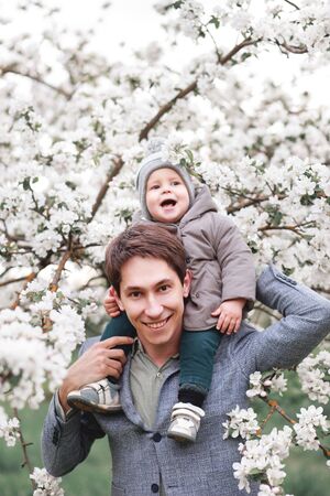 Happy little baby boy and his dad in a blooming Apple orchard in spring.
