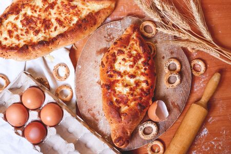 Top view of a delicious traditional Ajarian khachapuri-an open baked pie with melted salted Suluguni cheese and egg yolk on a wooden tray on the table during cooking. Traditional Georgian cuisineの写真素材
