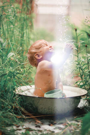 Sunny summer day.A charming little boy is bathing in a baby bath on a green lawn.He splashed and laughed.の写真素材