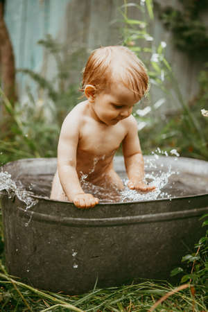 a little boy bathes in a basin in the summer in a green garden.の写真素材