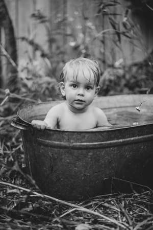 a little boy bathes in a basin in the summer in a green garden.の写真素材
