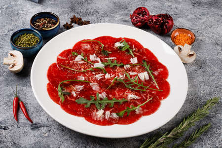 white dish with beef carpaccio with arugula on a gray table backgroundの写真素材